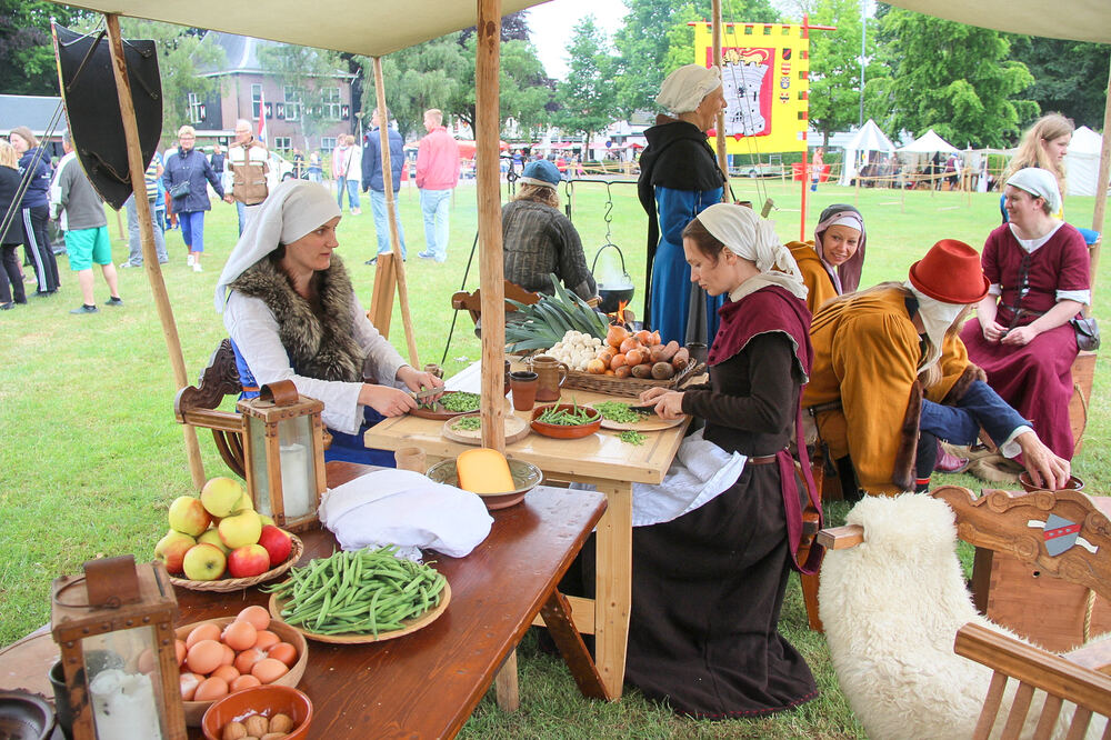 Deelnemers in middeleeuwse kleding bereiden groenten aan een houten tafel tijdens een historisch dorpsfeest