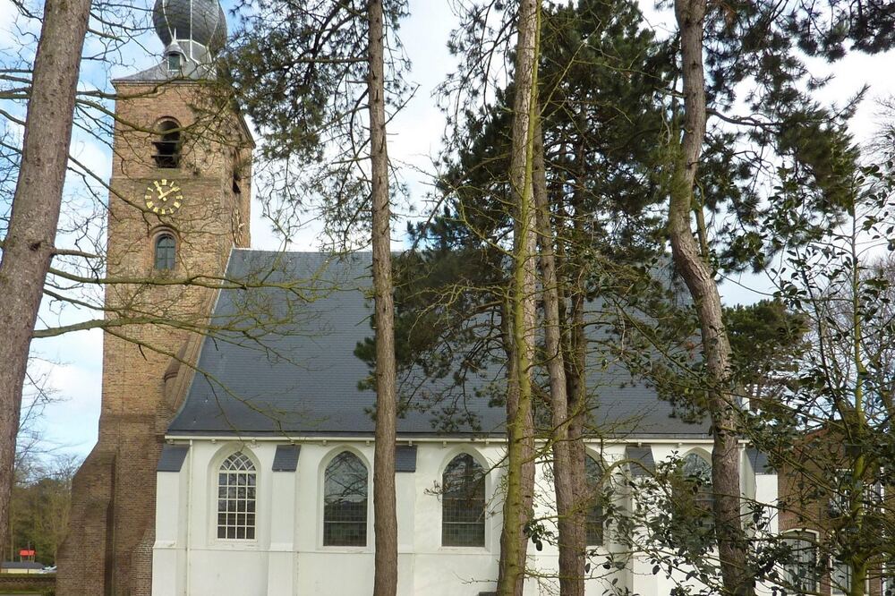 Witgepleisterde dorpskerk met klokkentoren tussen kale bomen in Oostvoorne