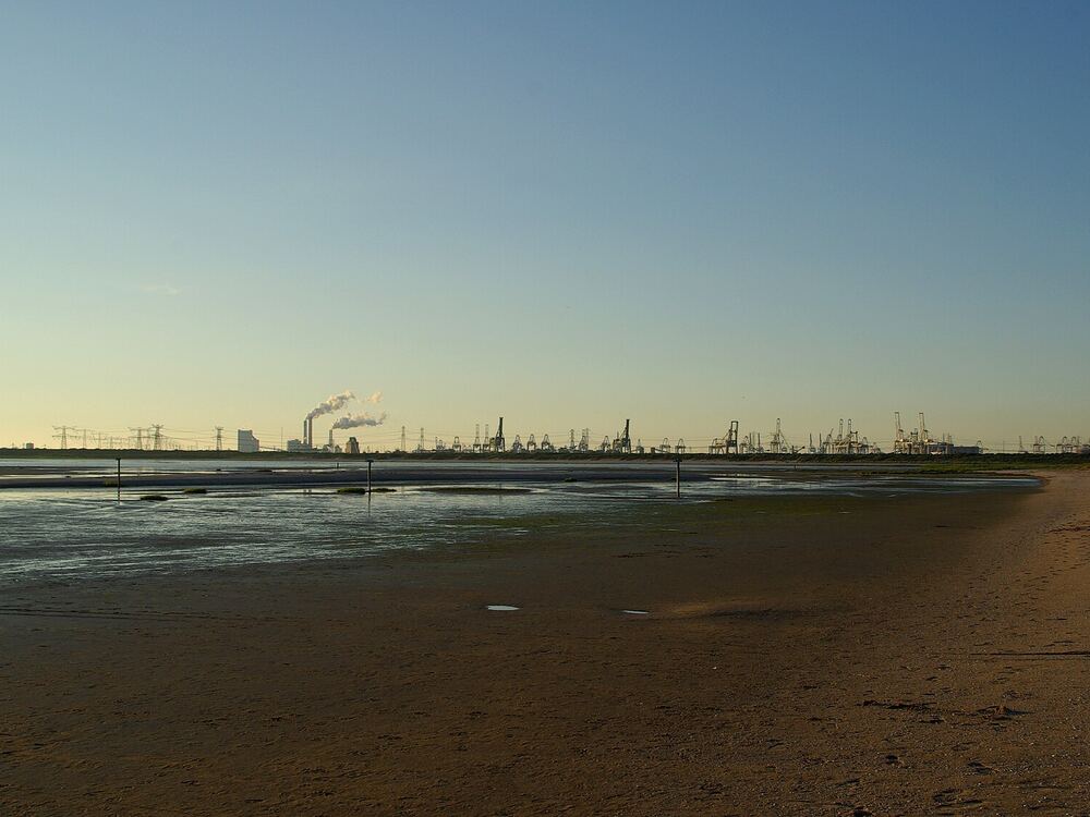 Leeg breed zandstrand bij eb met in de verte havenkranen aan de horizon